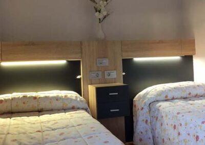 Habitación doble en Residencia Pirineos, residencia de mayores en Zaragoza con mobiliario moderno, iluminación integrada y entorno acogedor para el descanso.
